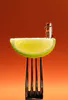 A staged photographic print of mini figure with surf board on lemon wedge and fork by New Zealand artist Adam Popovic, available at The Little Gallery Tairua